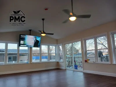 A newly finished sunroom addition features extensive windows, dark laminate flooring, two ceiling fans, and a wall-mounted television.