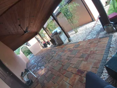 This image captures a covered outdoor patio featuring a wooden plank ceiling, recessed lighting, a decorative paver floor, and a stainless steel grill surrounded by gravel and bamboo.